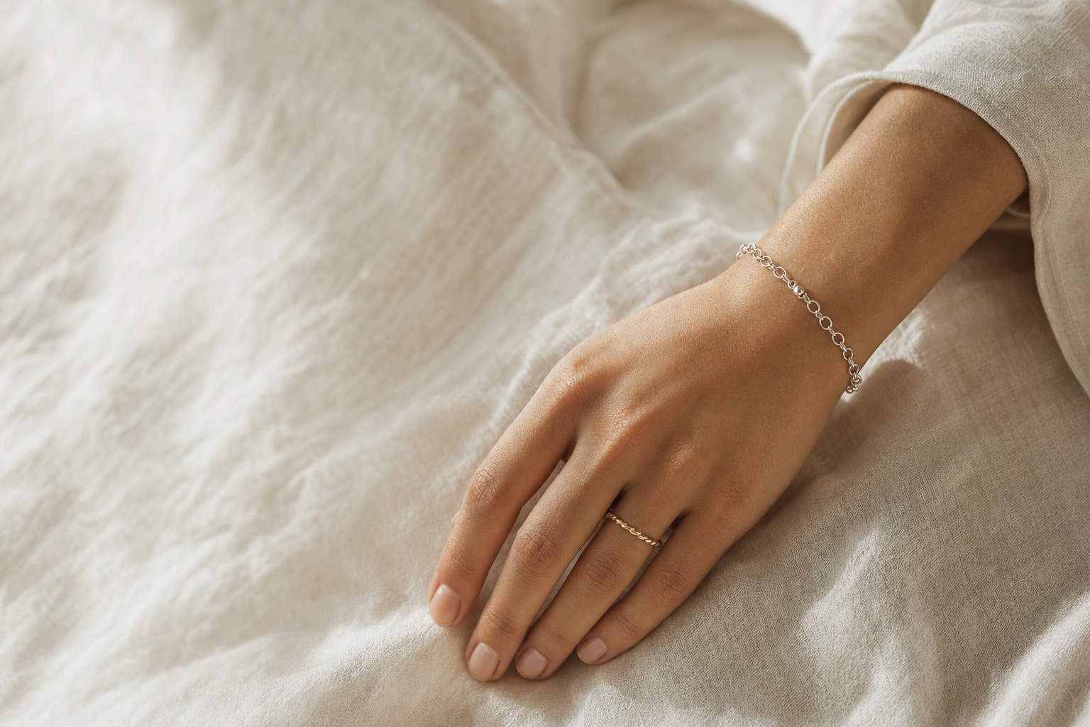 Woman's hand and wrist resting on linen, wearing a silver bracelet and gold ring